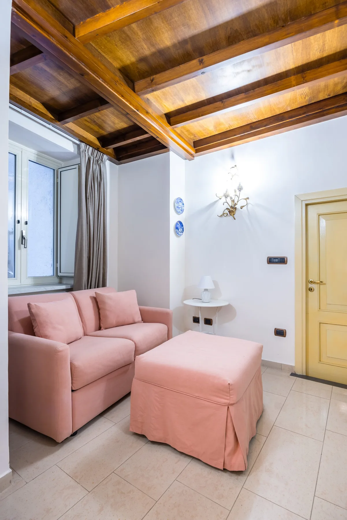 A sitting area with pink seating and a matching ottoman beneath exposed wooden ceiling beams.