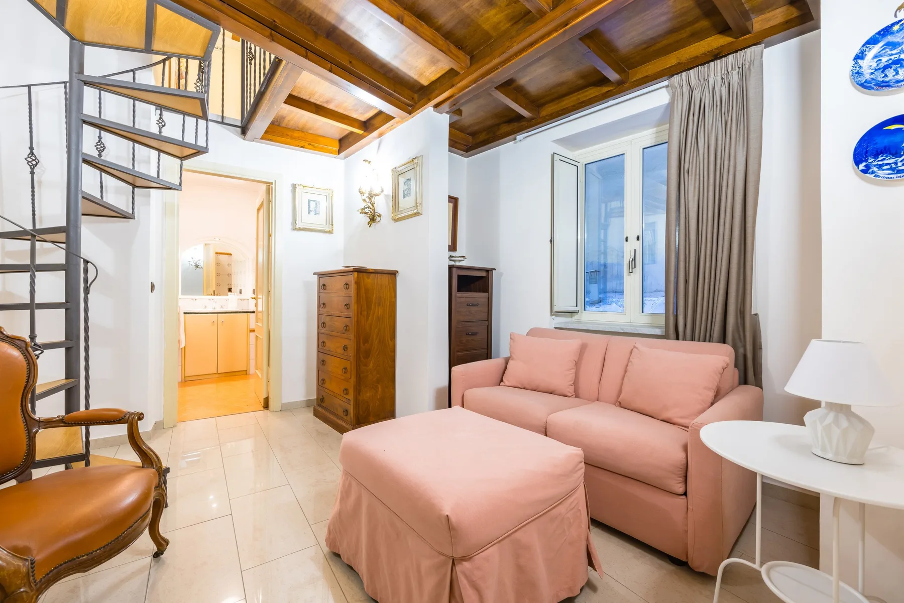 A living room with pink seating, a coffee table, and exposed wooden ceiling beams.