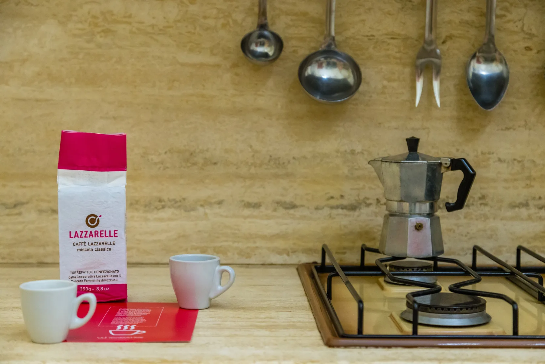 A kitchen counter with a coffee bag, cups, and a stovetop espresso maker.
