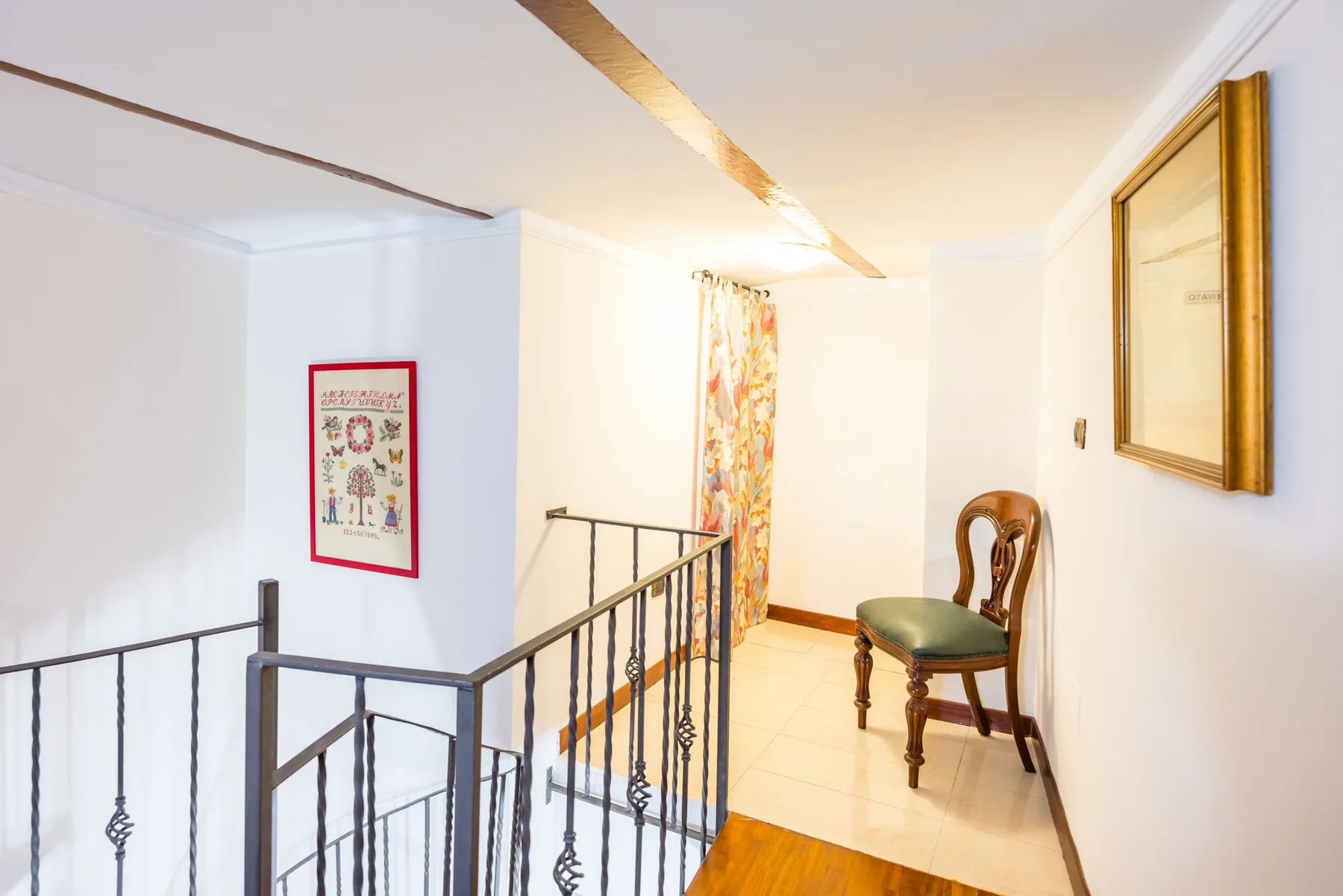 A bright upstairs landing with a dark metal railing and framed wall art.
