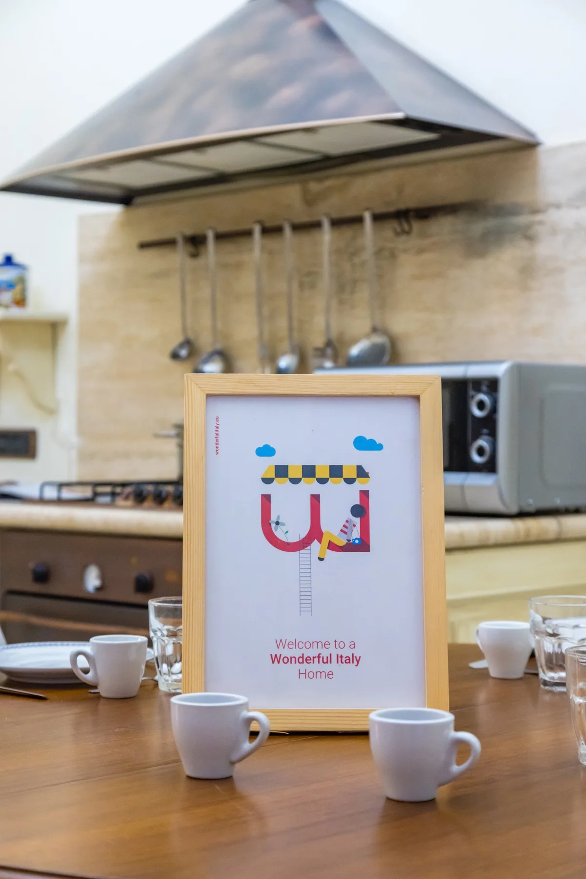 A framed illustrated sign sits on a wooden table in a kitchen.