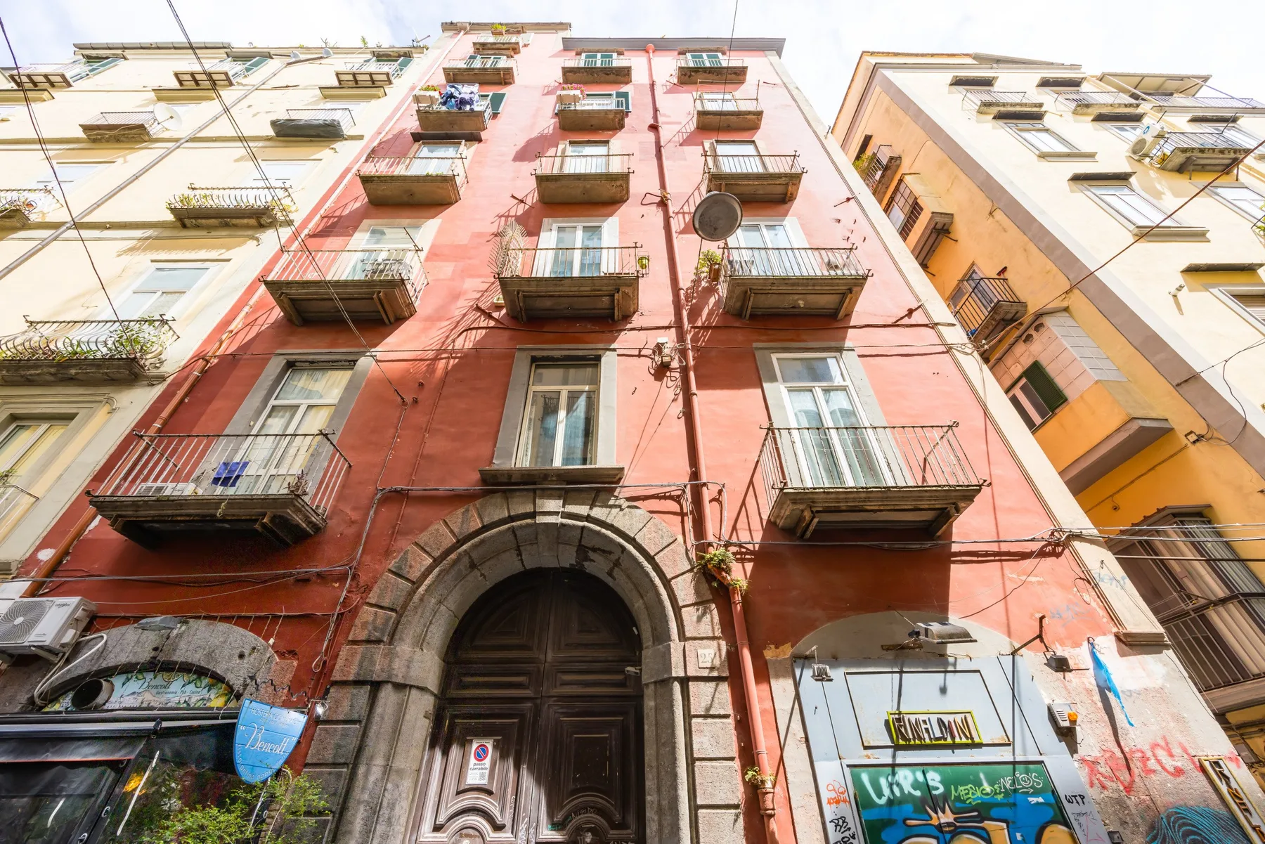 A red multi-story building façade with balconies and an arched entrance.