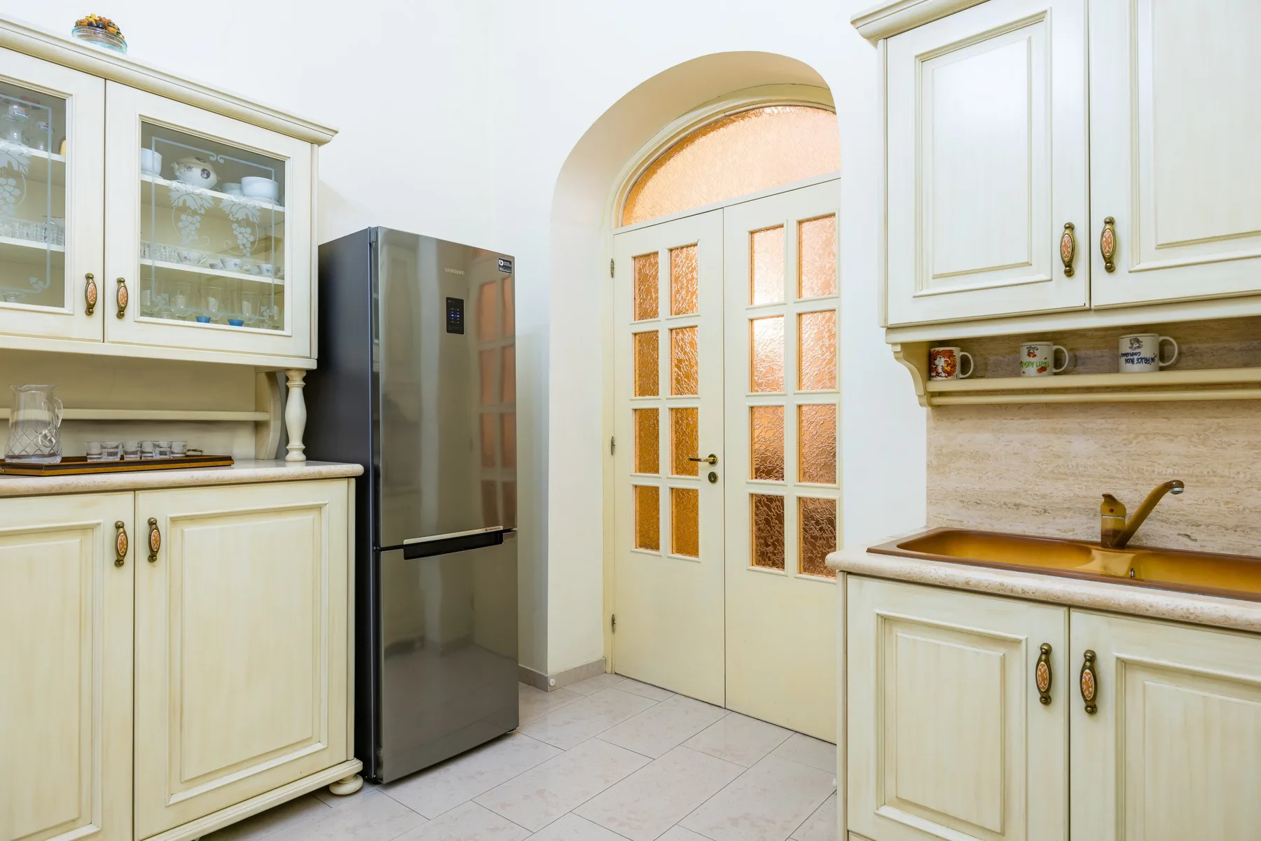 A bright kitchen with cream cabinets, a refrigerator, and a sink.