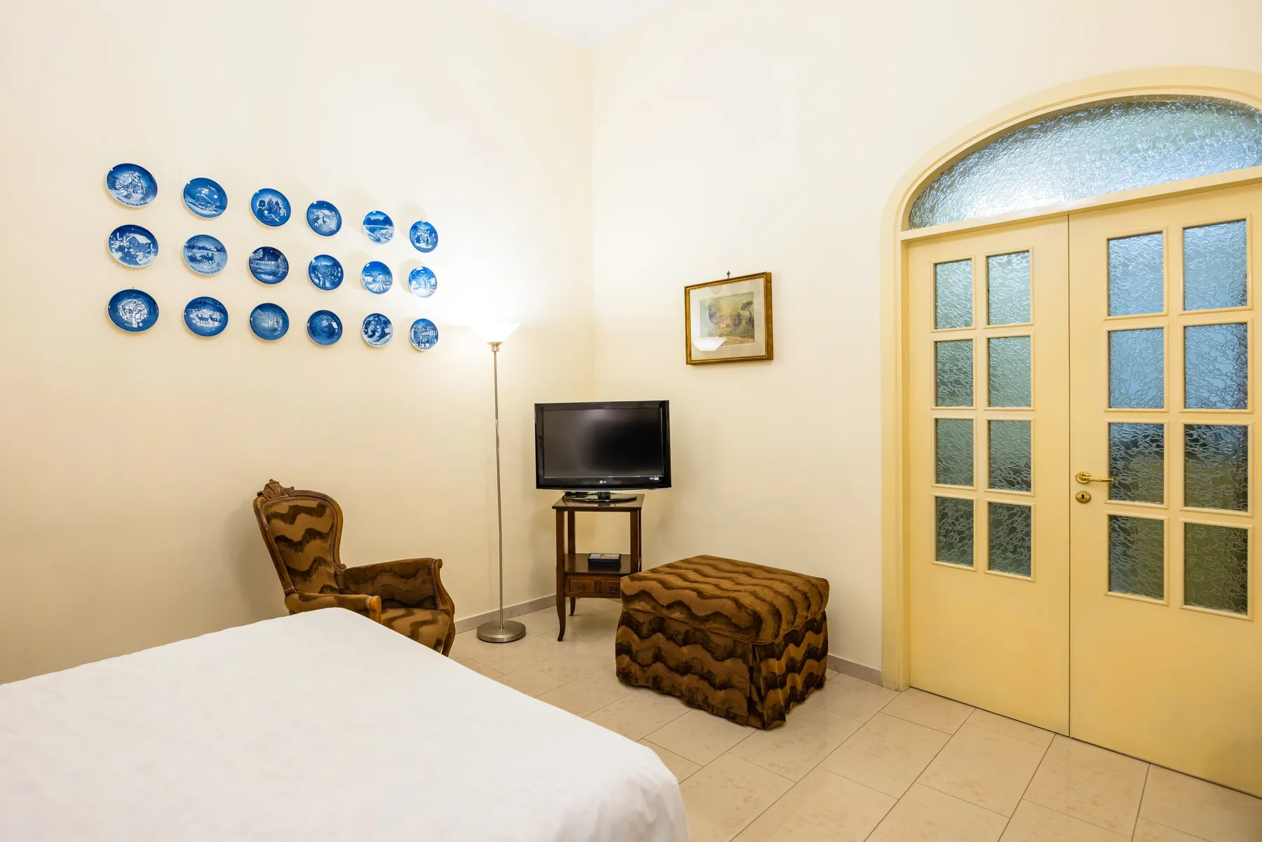 A bedroom with a bed, television, and seating beside glass-paneled double doors.