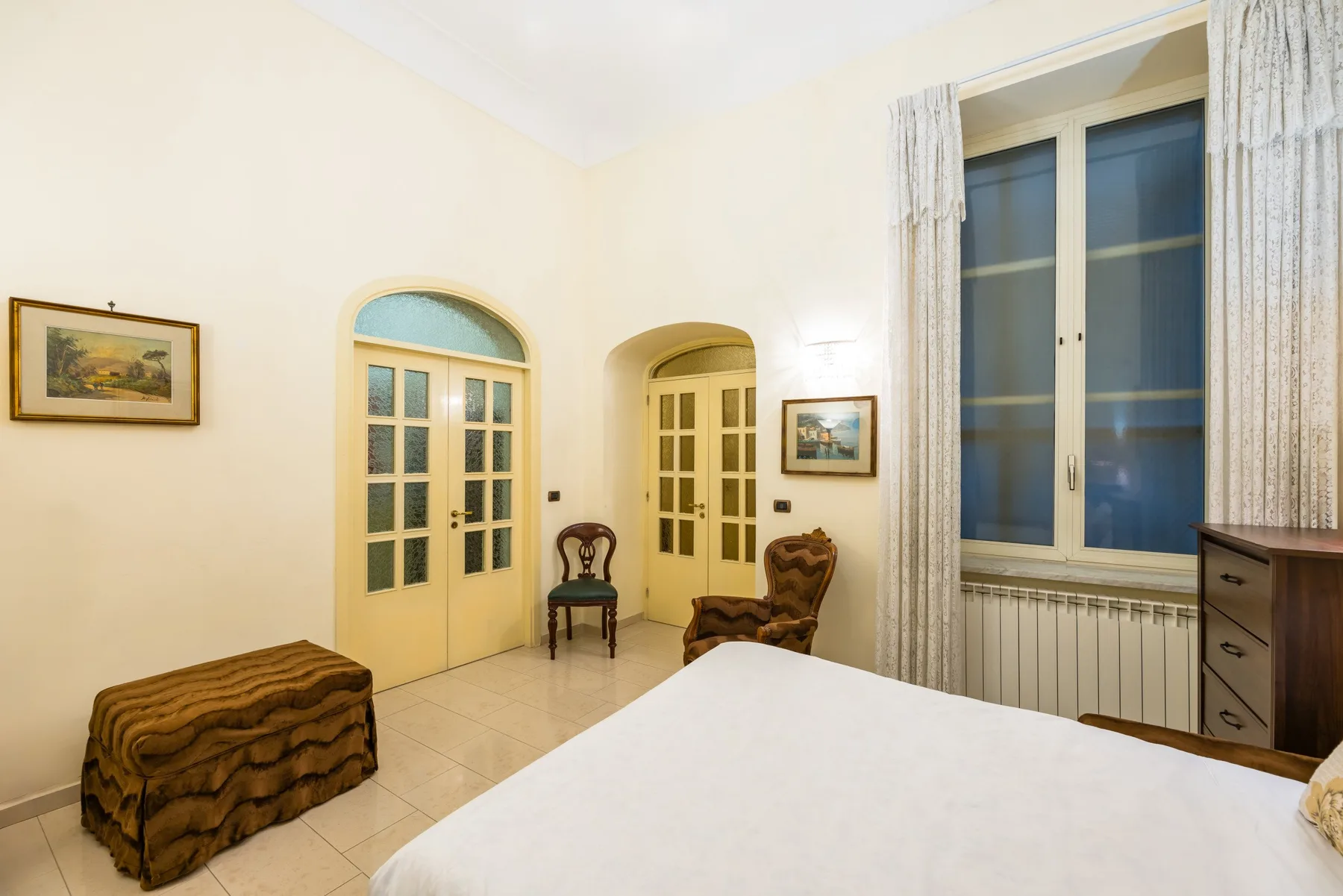 A bedroom with a bed, two arched doorways, and a large curtained window.
