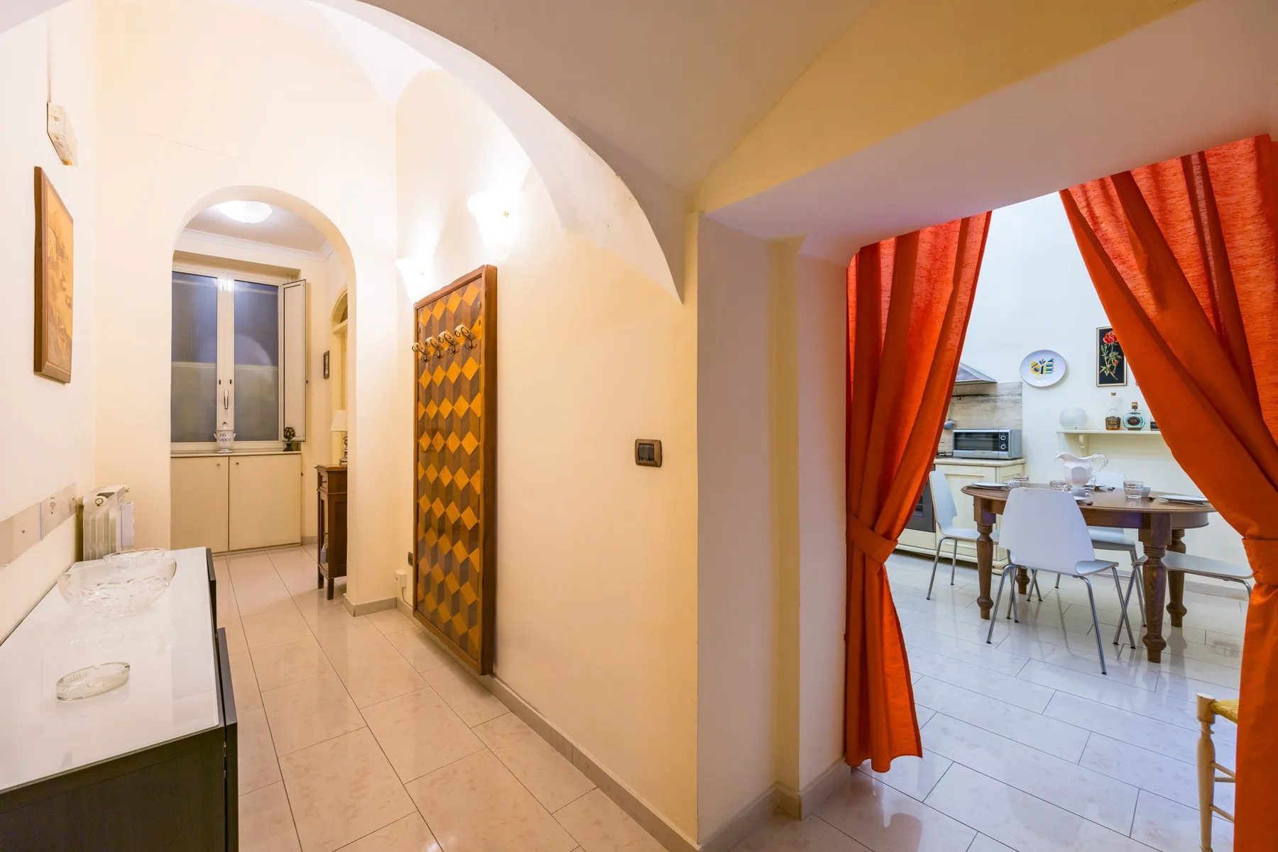A tiled hallway opens onto a dining area framed by bright orange curtains.