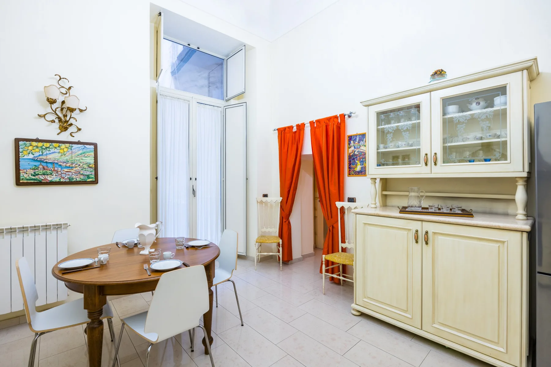 A bright dining area with a round table, chairs, and a large display cabinet.