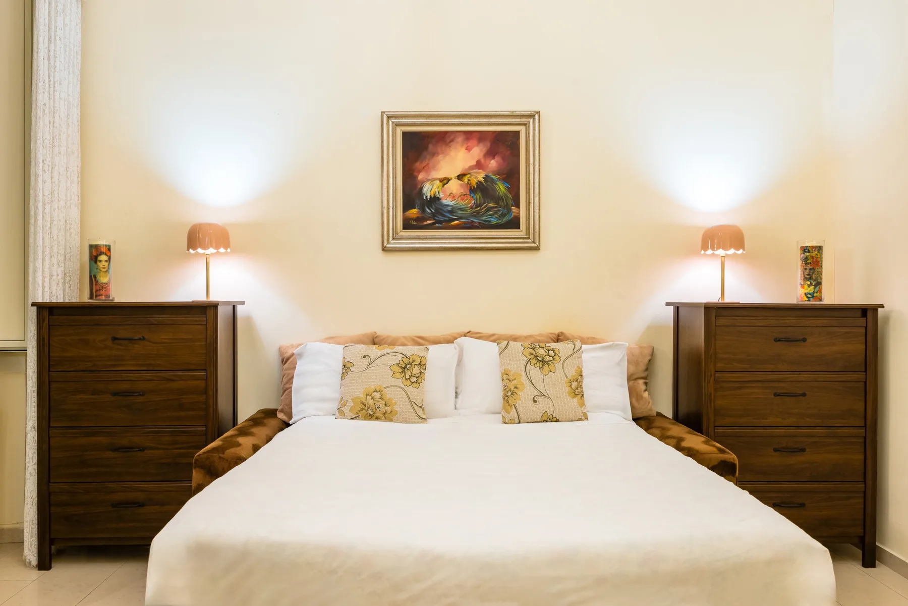 A bedroom with a neatly made bed, matching bedside chests, and warm lamps.