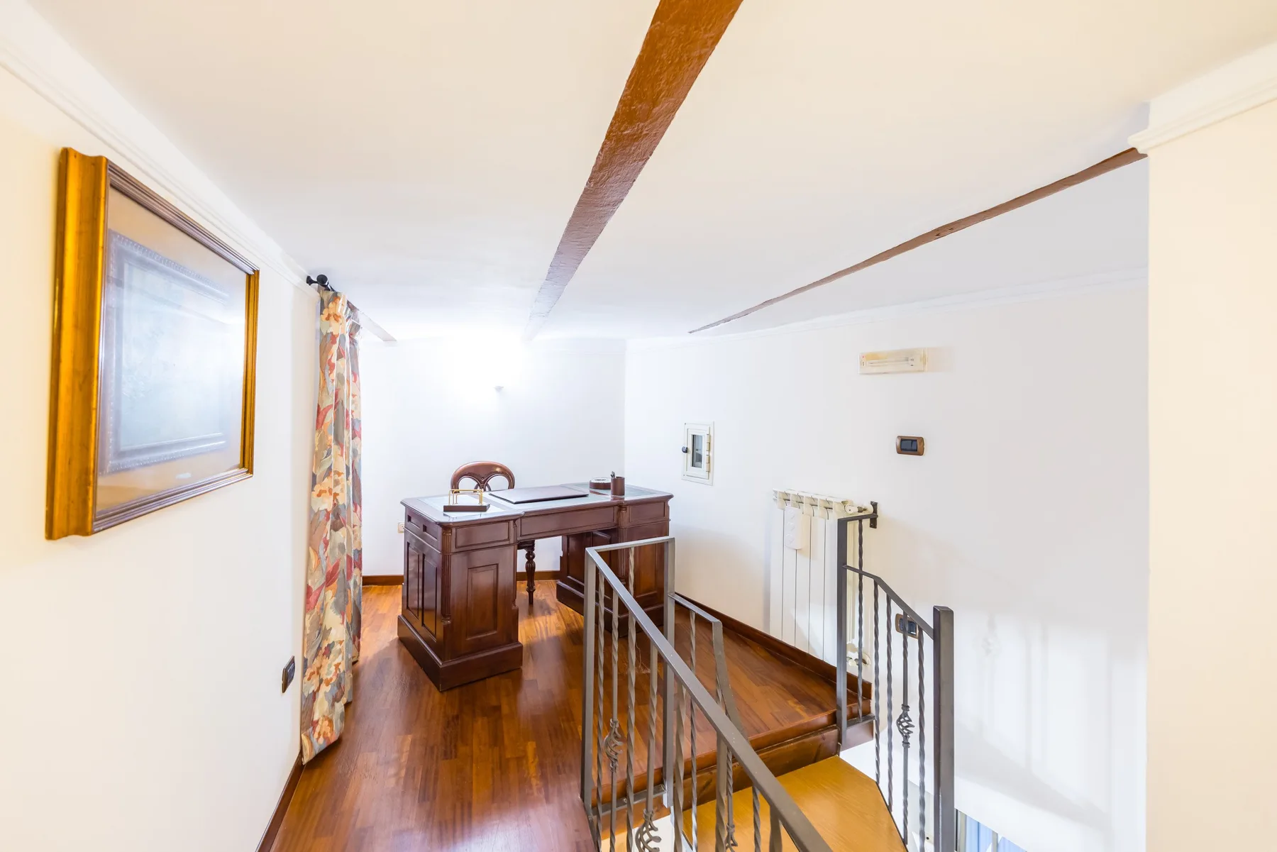 A wooden desk sits beside a stair railing in a bright interior landing.