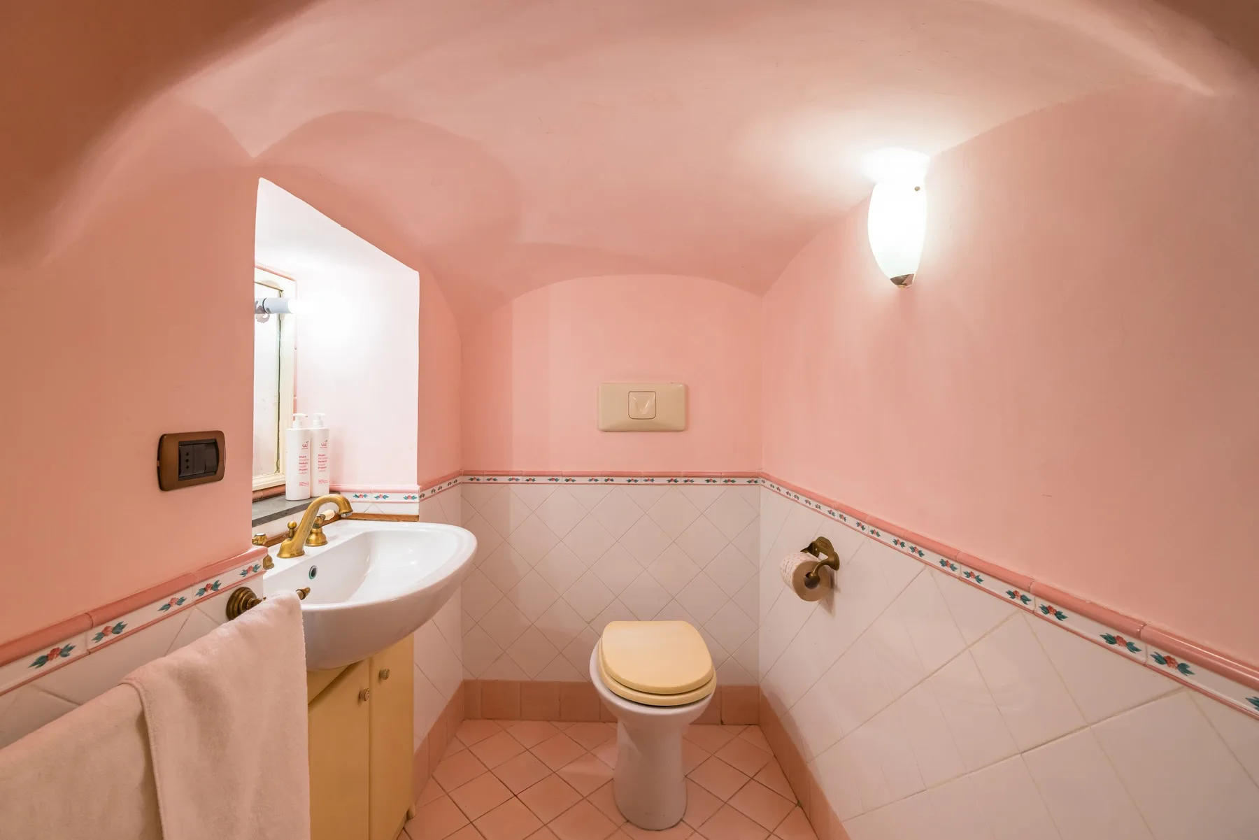 A small pink bathroom with a toilet, sink, and tiled walls.
