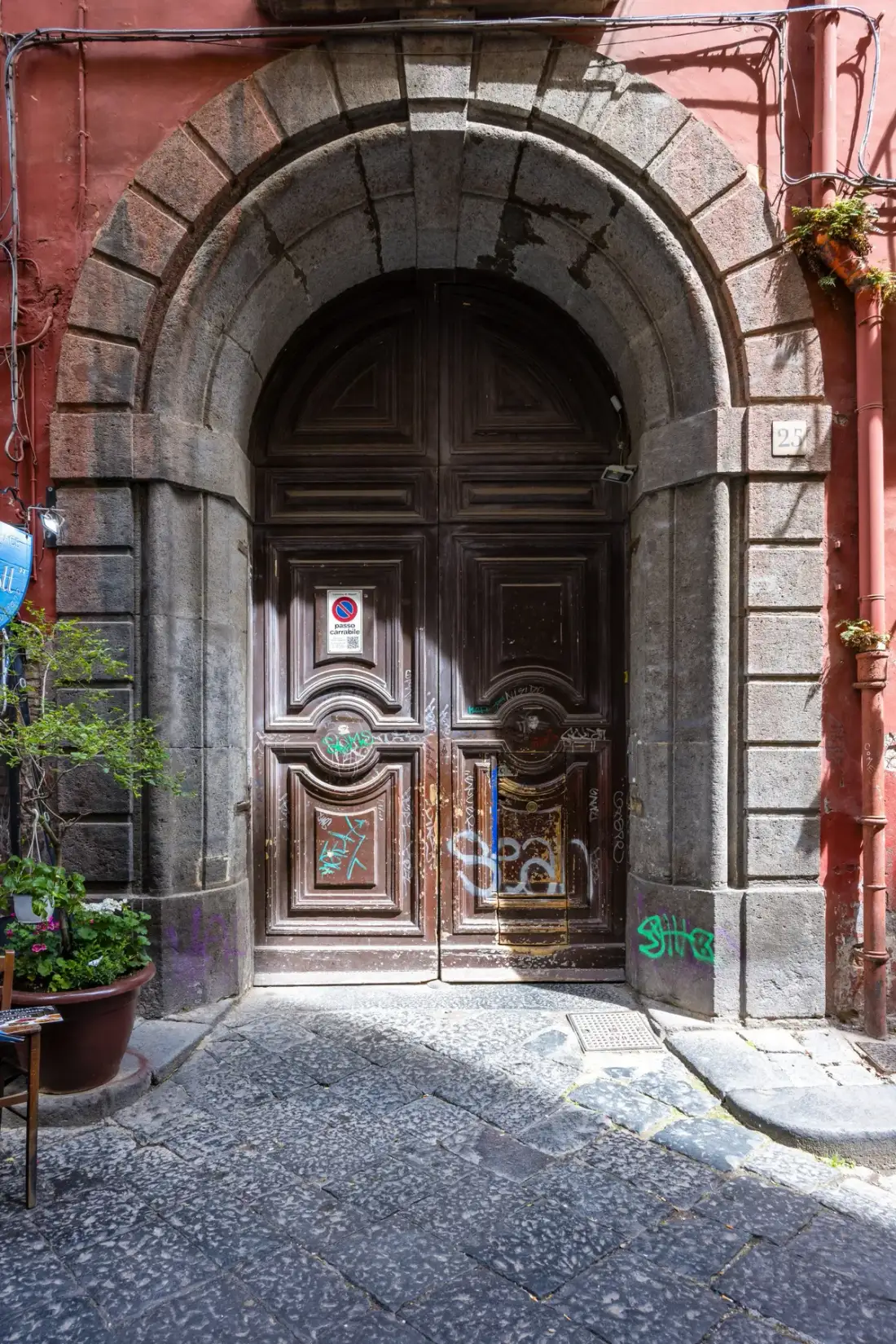 An ornate dark wooden entrance sits beneath a large stone arch on a narrow street.