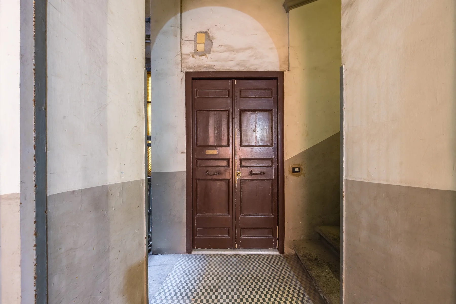 A narrow entrance hall with a dark wooden double door and patterned tile floor.