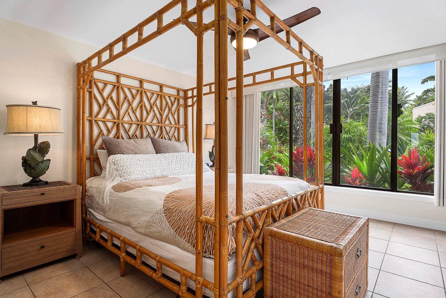 Un dormitorio con una cama enmarcada en bambú junto a una gran ventana con vegetación.