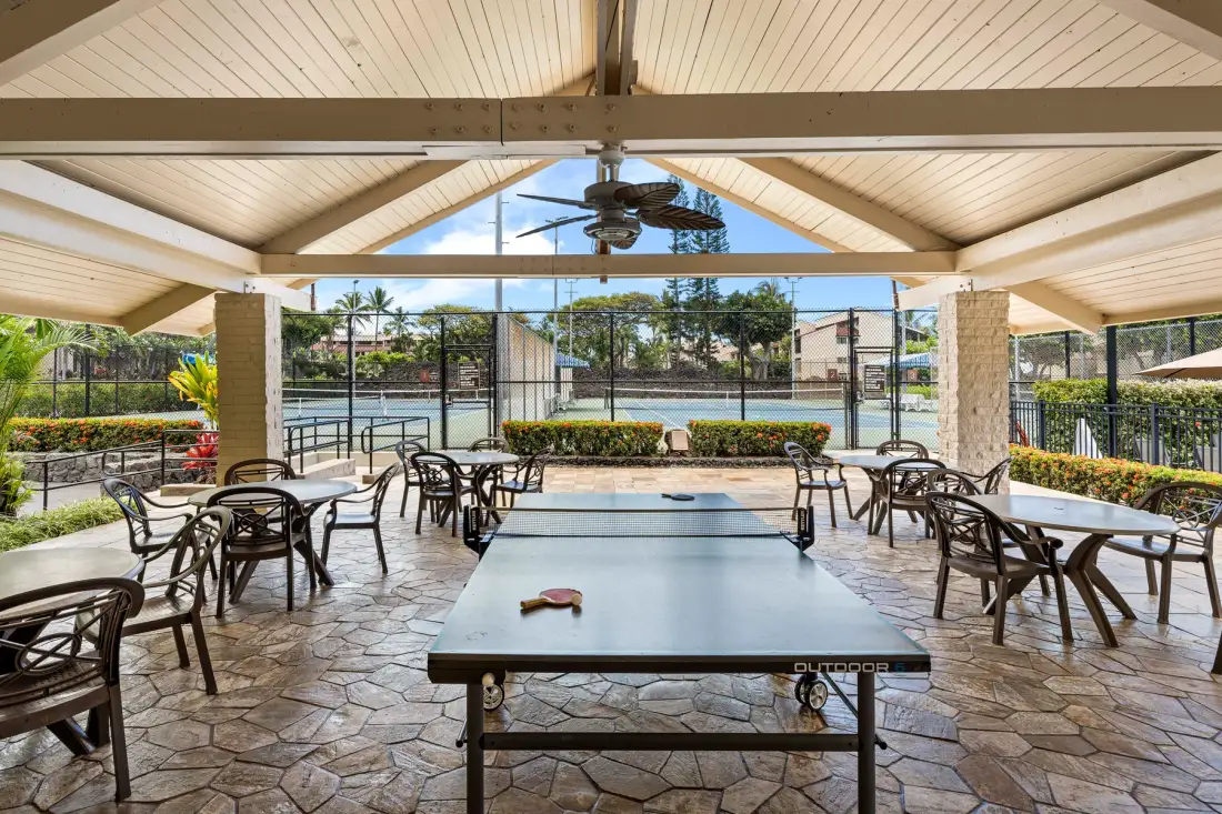 Una zona recreativa exterior cubierta con una mesa de billar y asientos frente a una piscina.