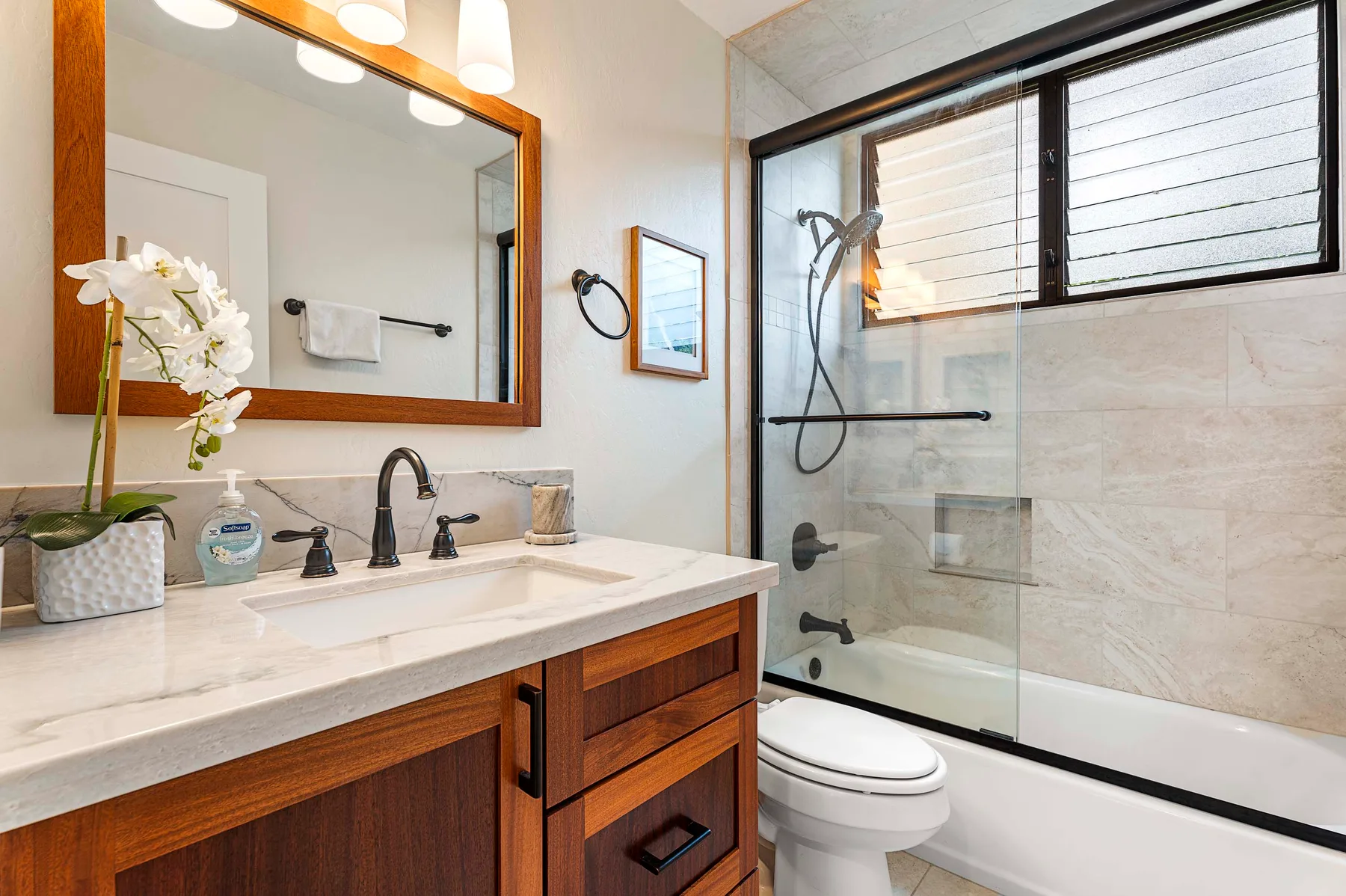 Un baño con tocador de madera, lavabo y ducha con mampara de vidrio.