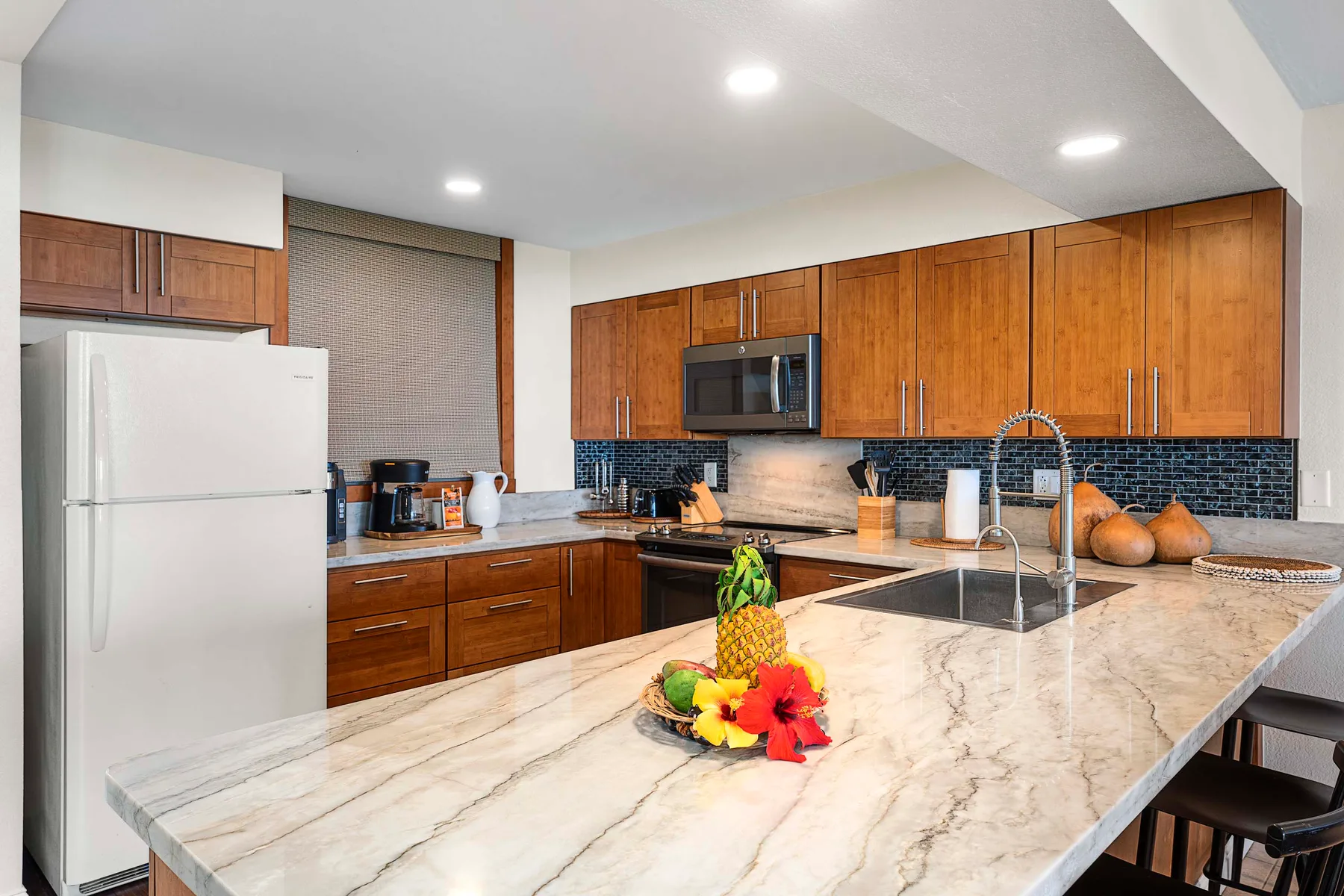 Una cocina con gabinetes de madera, un refrigerador y una amplia encimera de piedra.