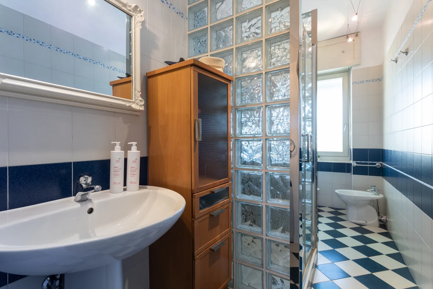 A tiled bathroom with a bathtub, glass-block partition, and toilet.