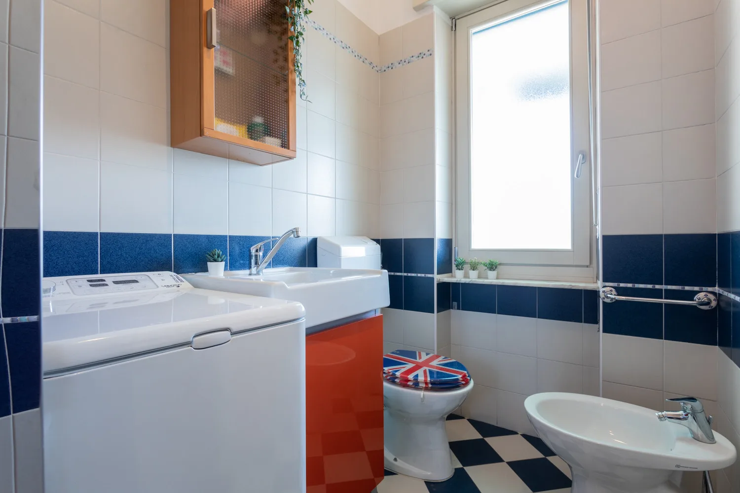 A tiled bathroom with a washing machine, sink, toilet, and bidet.