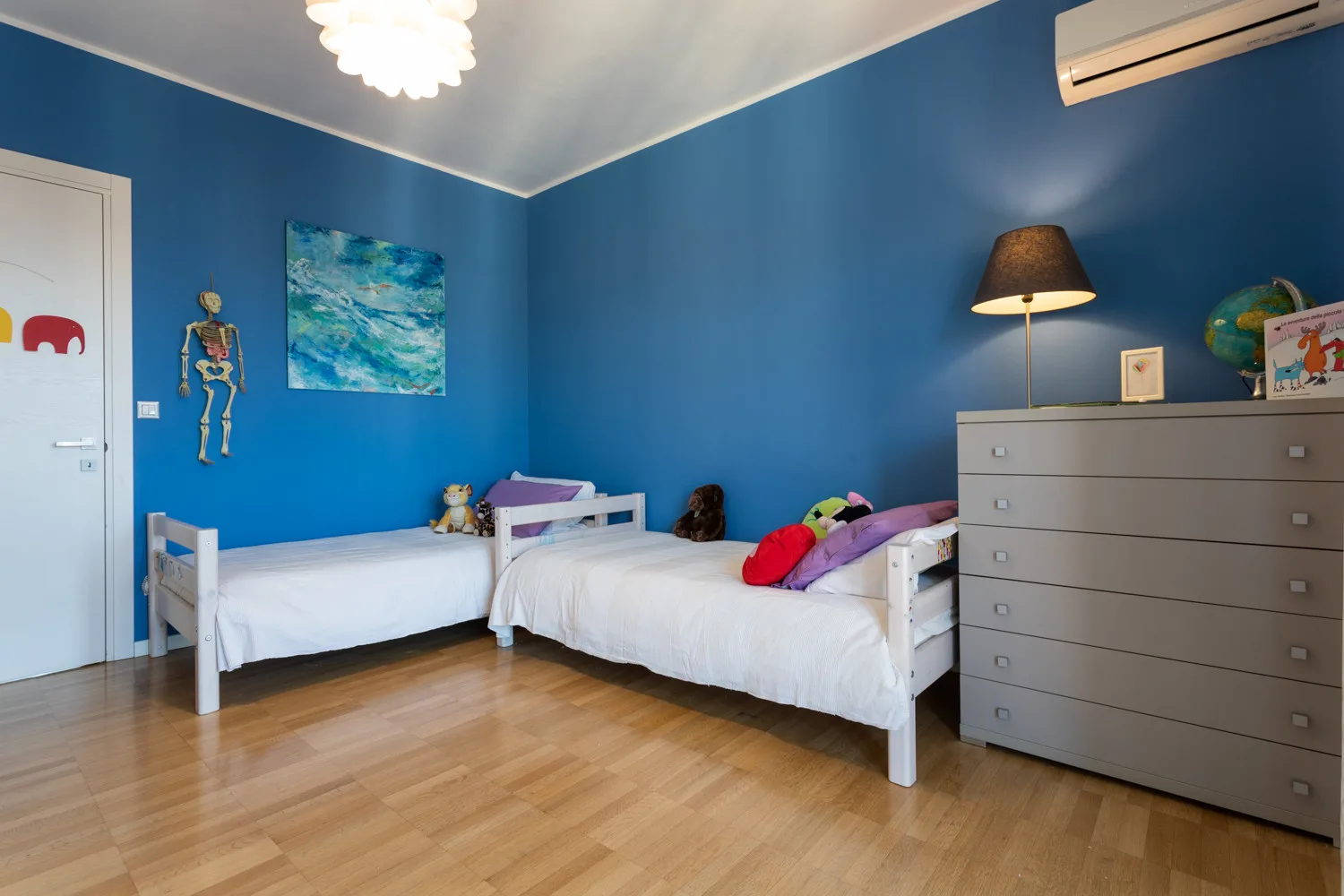 A blue-walled bedroom with two beds and a dresser.