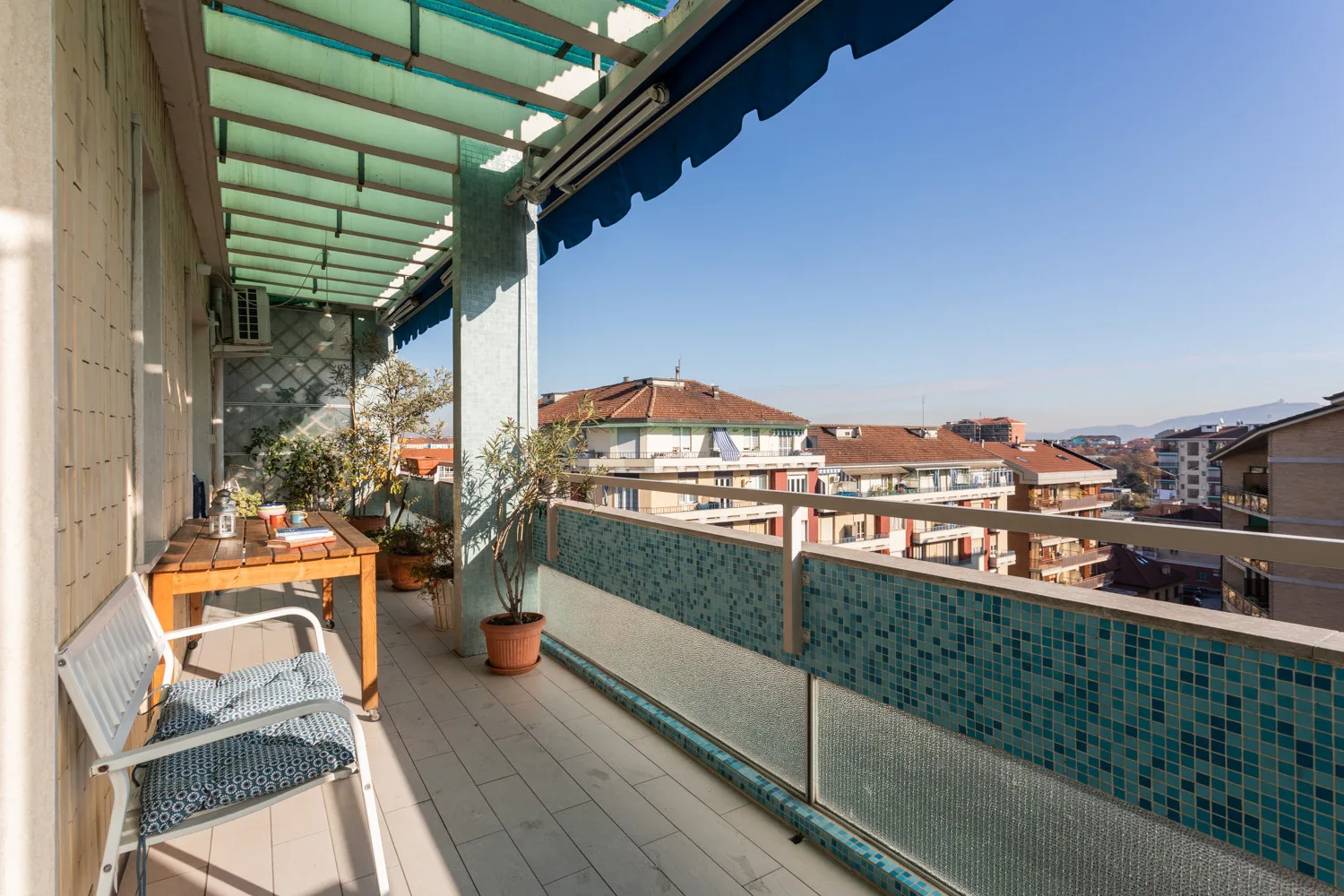 A covered balcony with seating and a view of nearby rooftops.