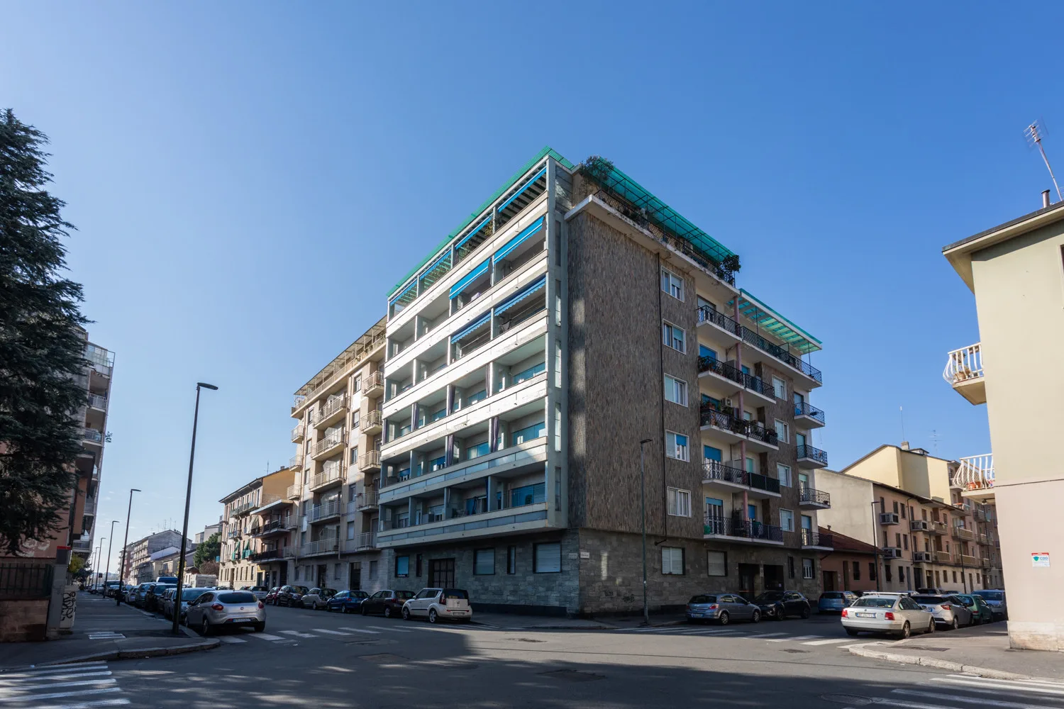 A multi-story apartment building stands at a street corner under a clear sky.