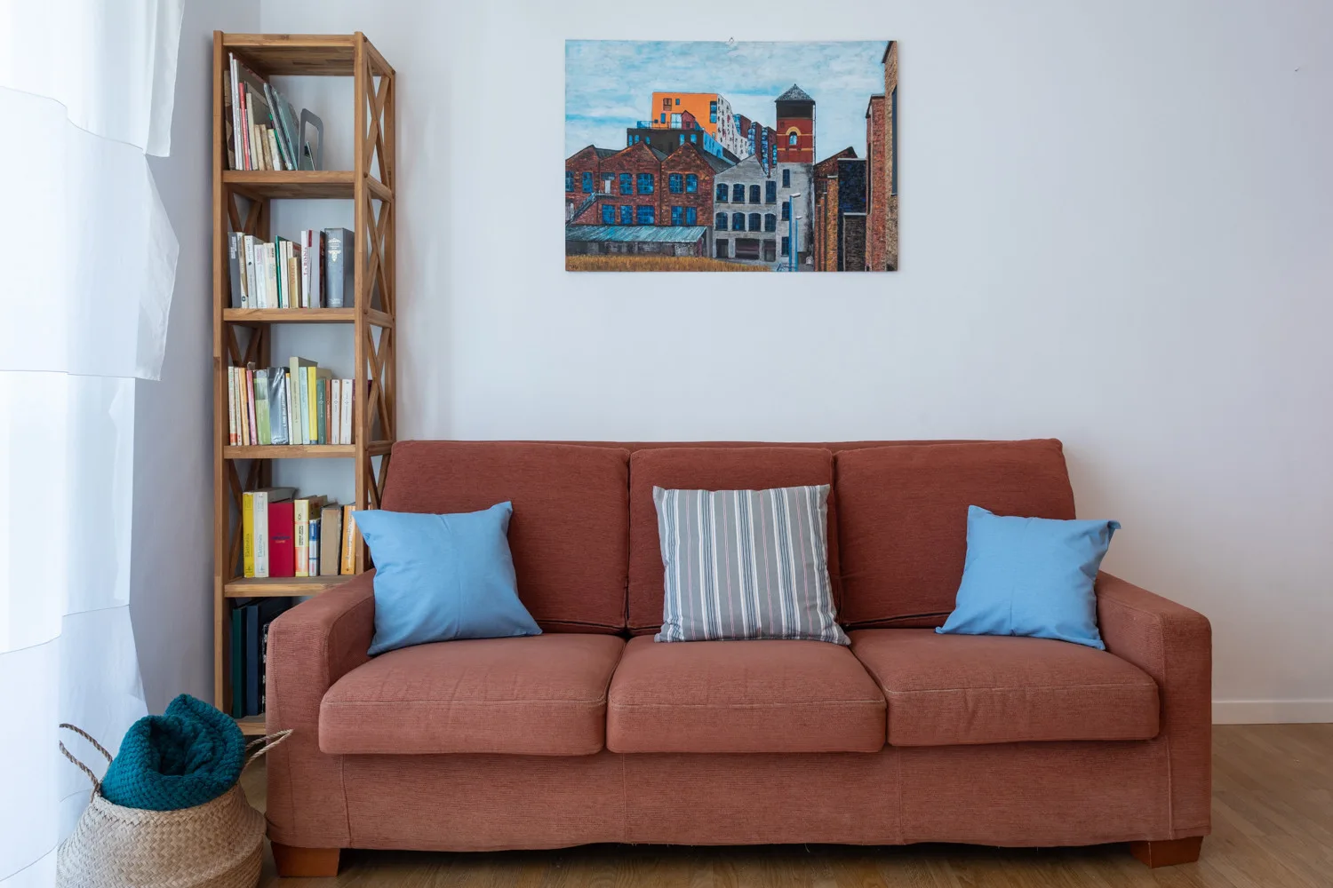 A living room with a rust-colored sofa, bookshelves, and a framed cityscape.