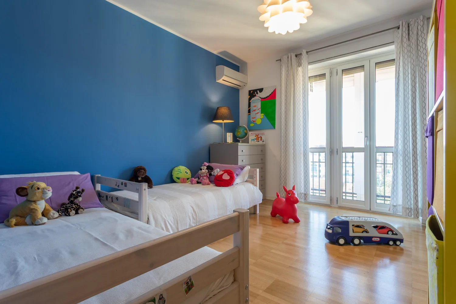 A children’s bedroom with two beds, toys, and a large glass balcony door.
