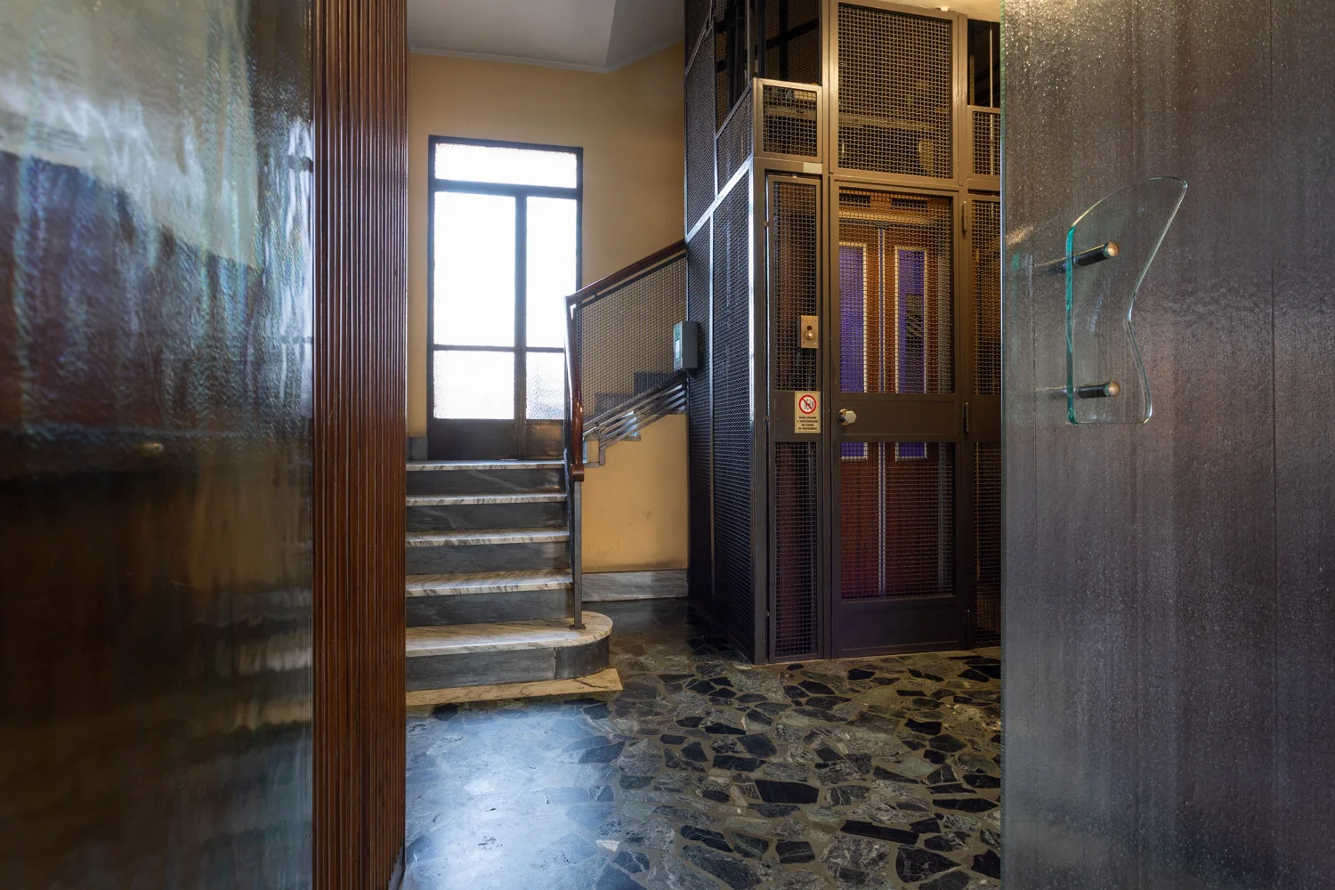 An interior hallway with a staircase and a tall metal elevator gate.