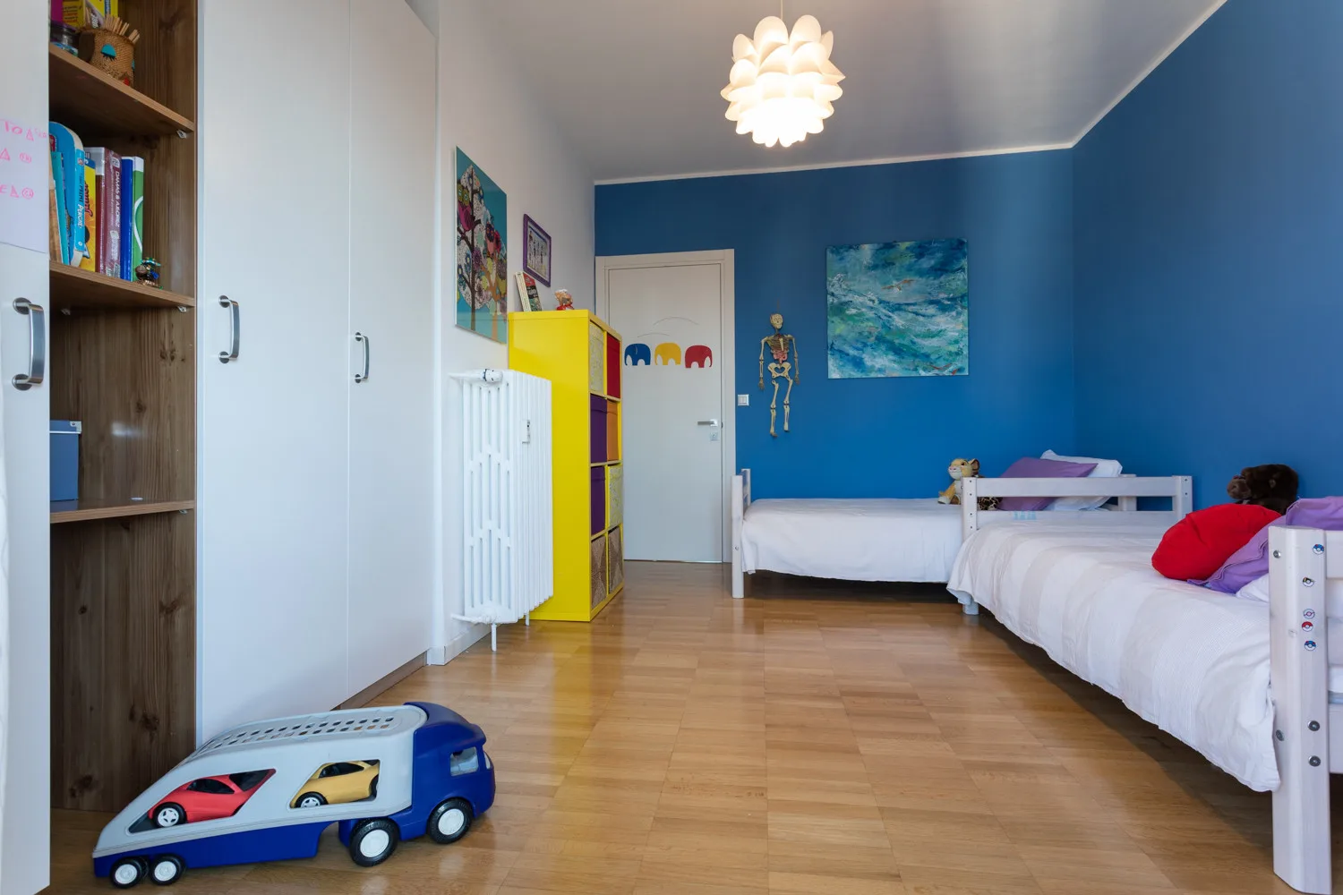 A children’s bedroom with two beds, colorful storage, and a blue accent wall.