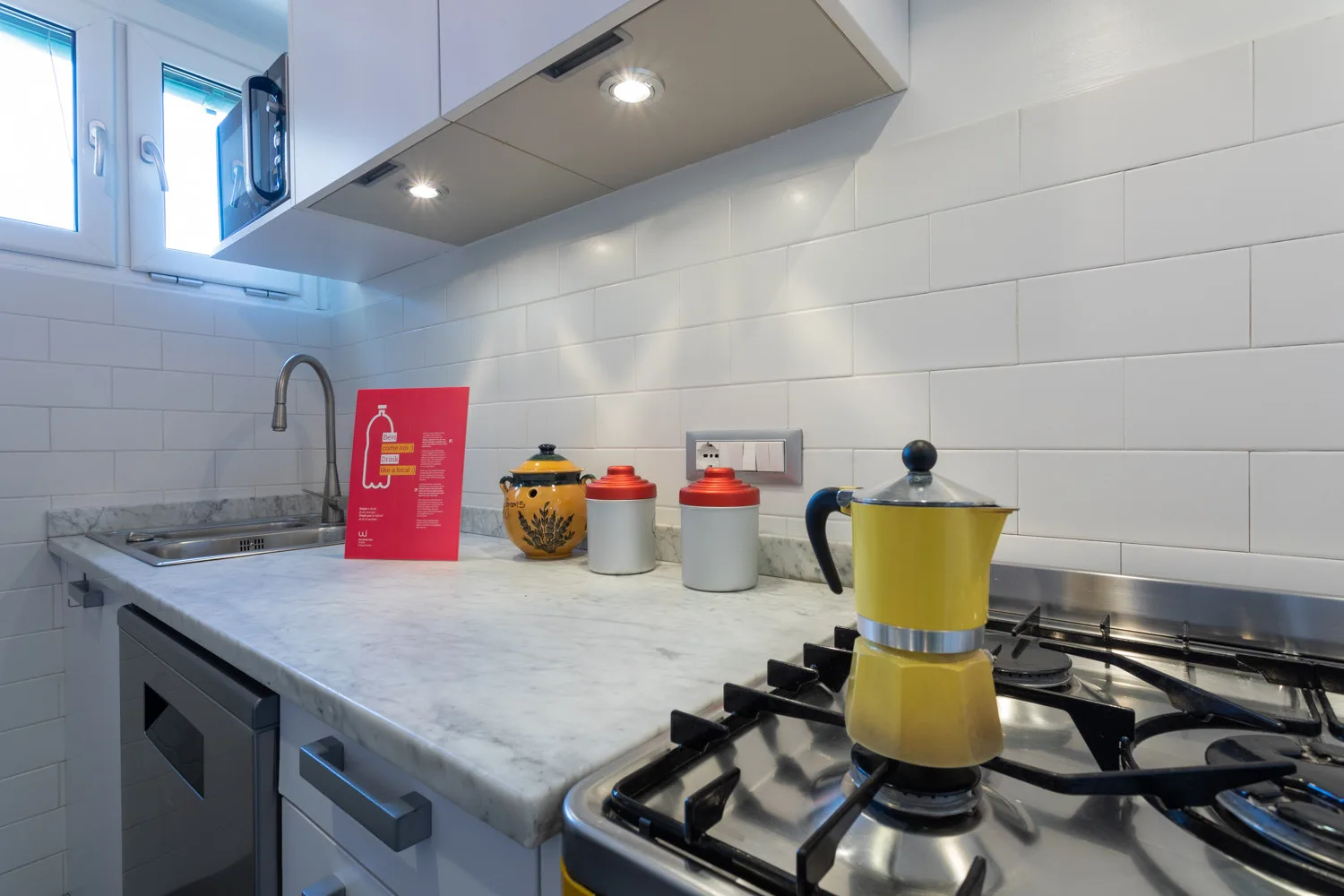 A modern kitchen counter with a sink, tiled backsplash, and stovetop.