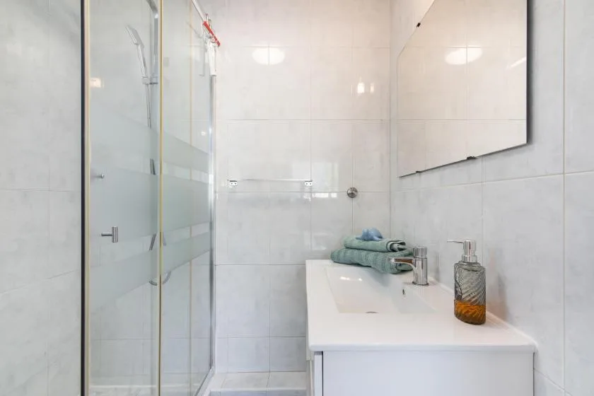 A tiled bathroom with a glass shower and a white sink vanity.