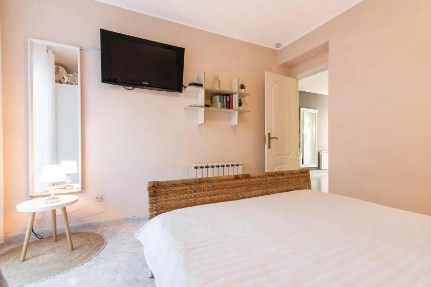 A bedroom with a bed, wall-mounted television, and small bedside table.