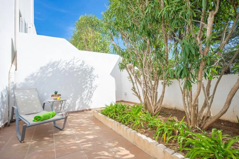 A tiled outdoor patio with seating beside a leafy garden.