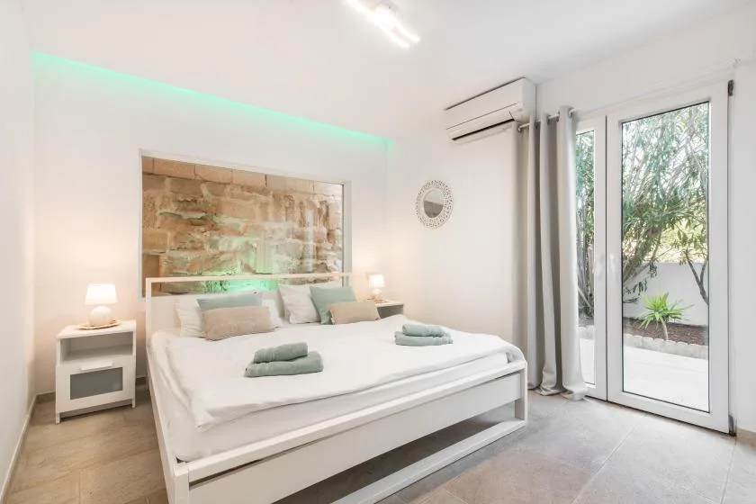 A bright bedroom has a neatly made bed beside glass doors opening onto a patio.