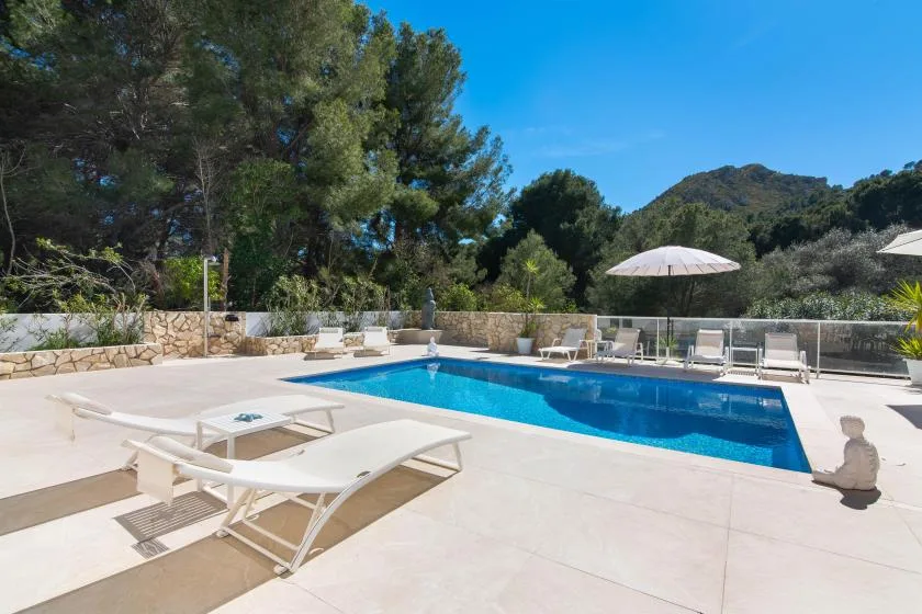 An outdoor swimming pool is surrounded by pale paving and lounge seating.