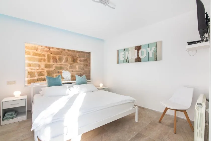A bright bedroom with a white bed and a chair beside the wall.
