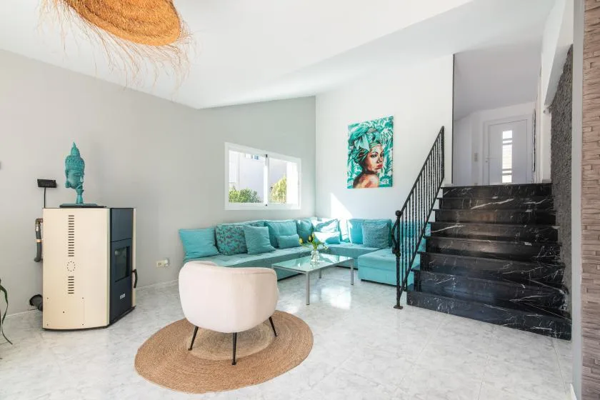 A bright living room with turquoise seating and a staircase along the right wall.