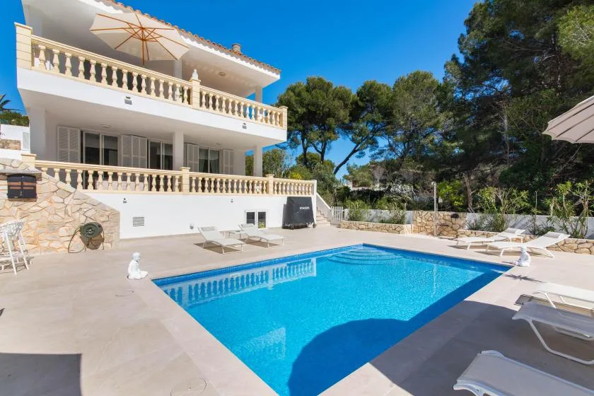 An outdoor swimming pool beside a white villa and sun loungers.