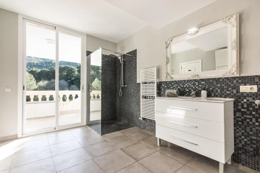 A bright bathroom with a glass shower, white vanity, and large window.