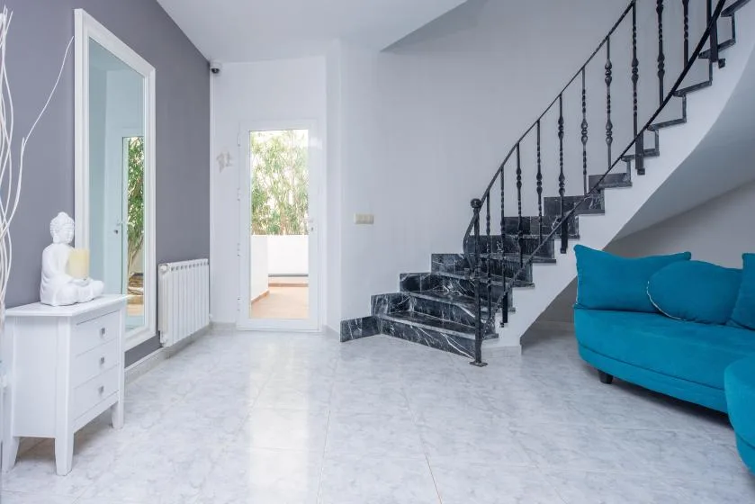 A bright living area with a staircase, white tile flooring, and a blue sofa.