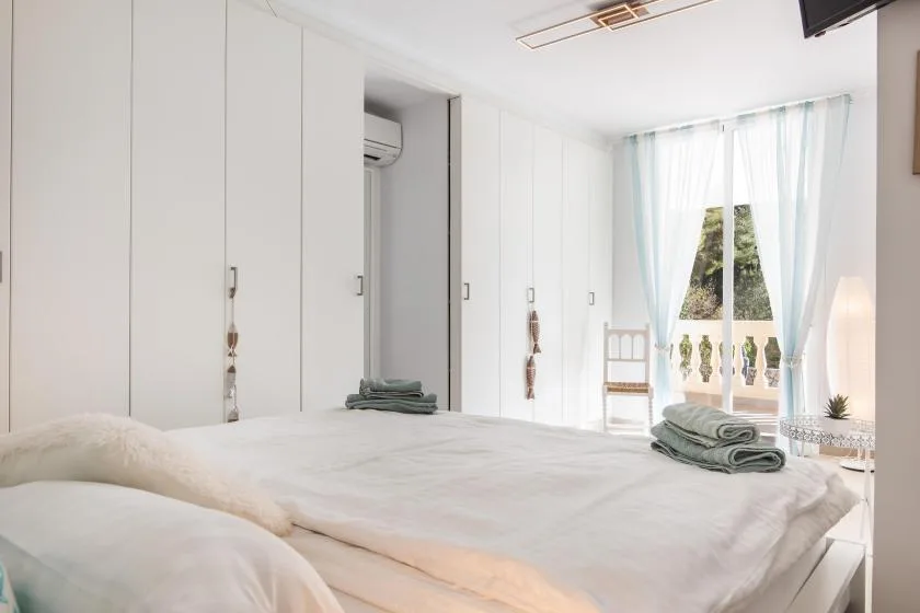 A bright bedroom with a bed, built-in cabinets, and a window with sheer curtains.