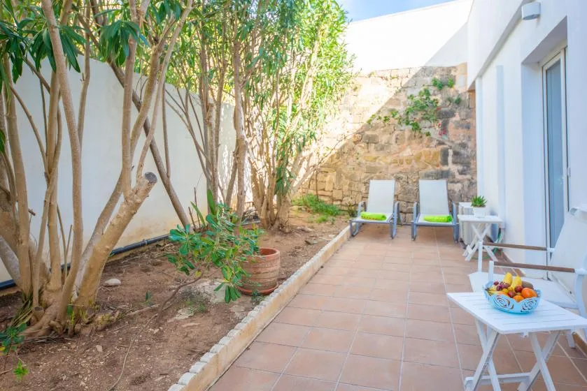 A tiled outdoor patio with lounge chairs beside a garden and stone wall.