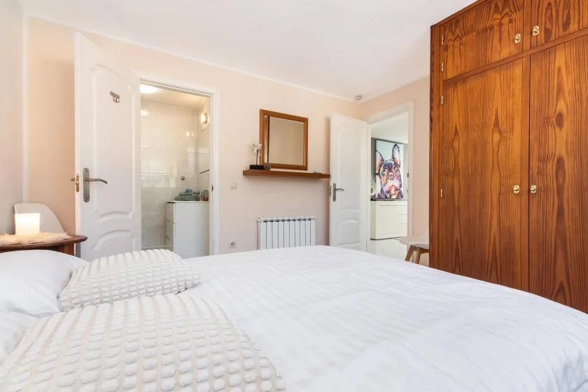 A bedroom with a bed, a wooden wardrobe, and a doorway to a bathroom.