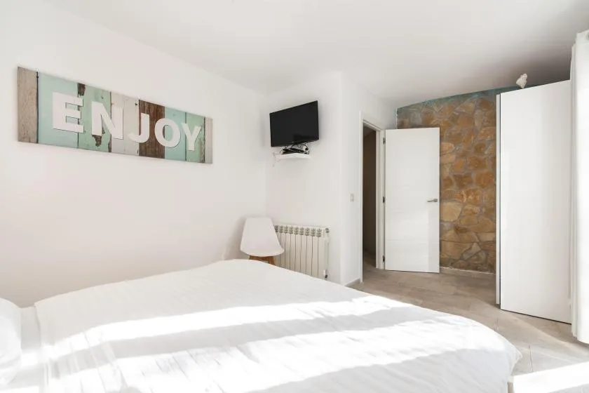 A bright bedroom with white bedding, a wall-mounted television, and an open doorway.