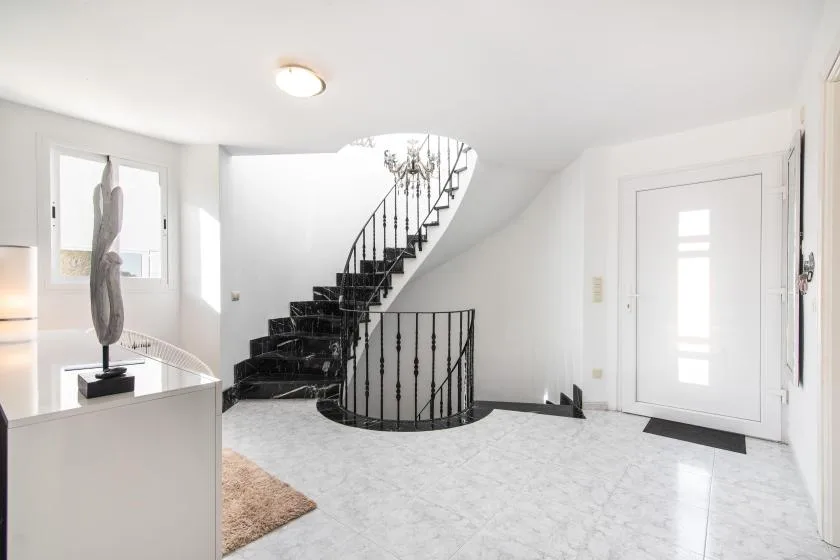A bright entry hall features a curved black staircase and a white front door.