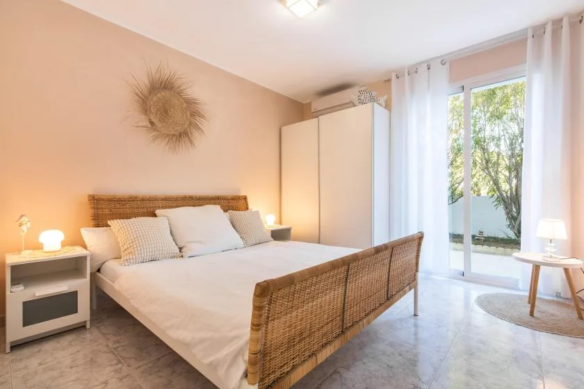 A bright bedroom with a woven bed frame and glass doors opening onto greenery.