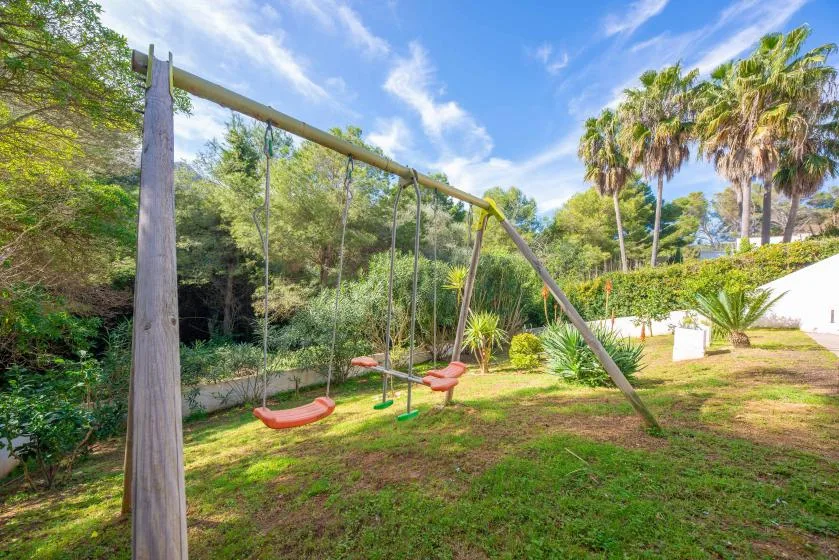 A garden play area with swings among trees and palms.