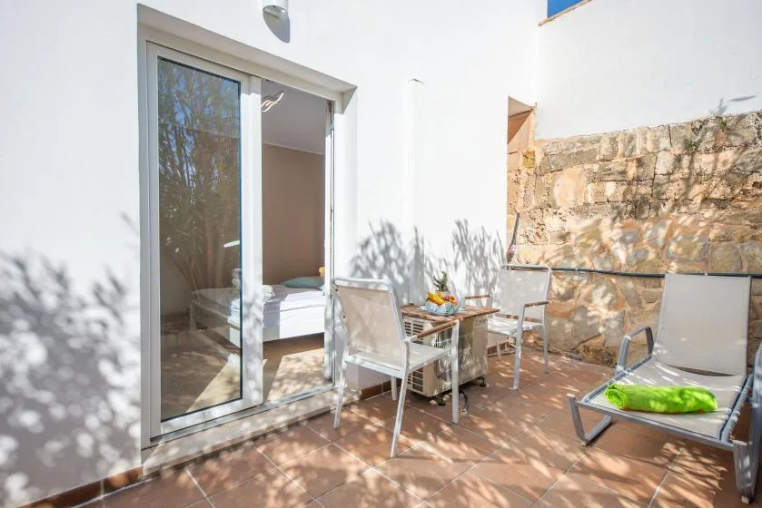 A sunlit patio with a small dining table and outdoor seating beside a bedroom.