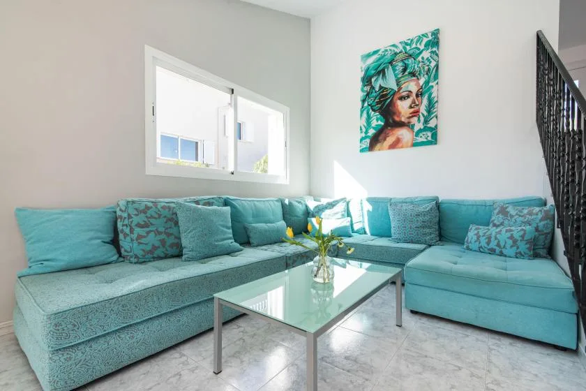 A bright living room with turquoise seating and a glass coffee table.