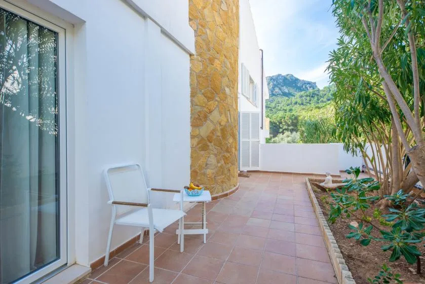 A tiled outdoor patio beside a white building, with seating and a planted garden.